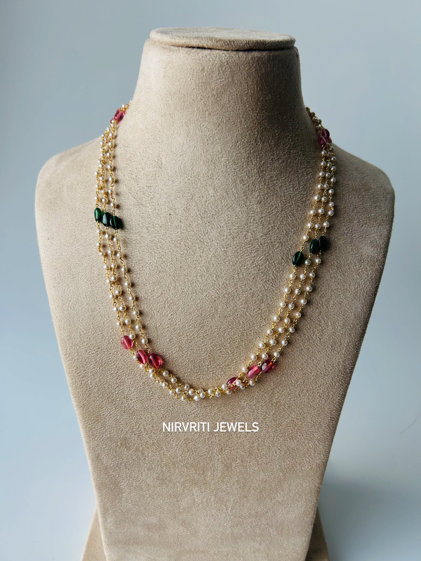 Graceful three-layer pearl necklace accented with ruby-red and emerald-green beads for timeless elegance.