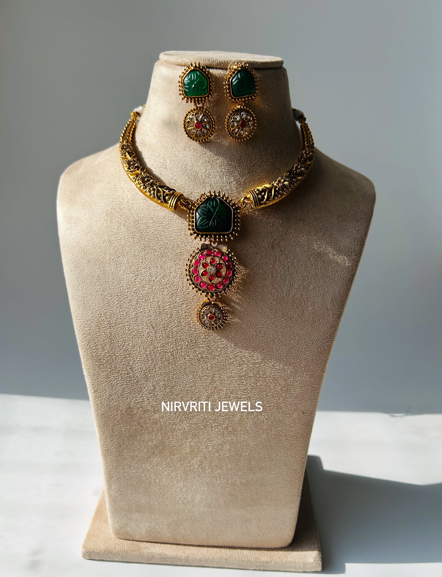Elegant antique-style necklace set with green stone carving and intricate ruby-studded floral motifs.